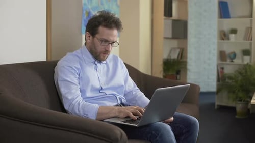 Nachdenklicher männlicher Wissenschaftler schreibt neuen Artikel auf Laptop, freiberufliche Arbeit