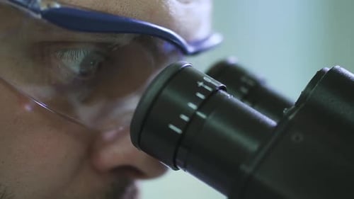 Man Looks Through Microscope in Science Lab Close Up