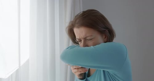 Woman Coughing into Elbow Indoors in Daytime