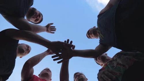 Teammates Putting Hands Together Against Blue Sky
