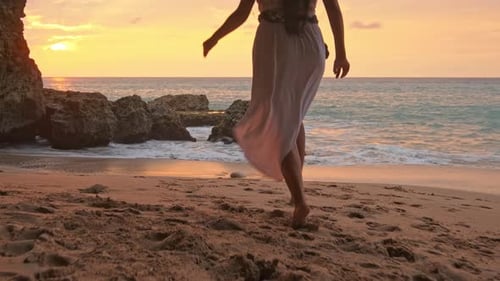 Brünette Frau in einem Kleid, das bei Sonnenuntergang oder Sonnenaufgang am Wasser entlang läuft. Glückliche sorglose Frau beim Tanzen