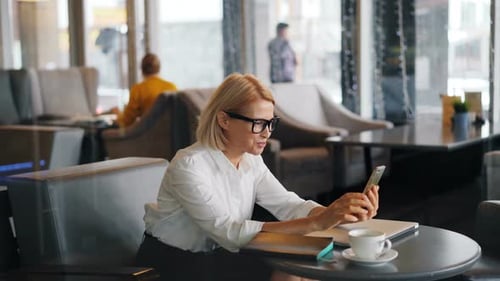 Cheerful Woman Entrepreneur Making Online Video Call in Cafe Talking Waving Hand