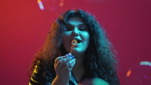 Woman Blowing Colorful Bubbles on Pink Background