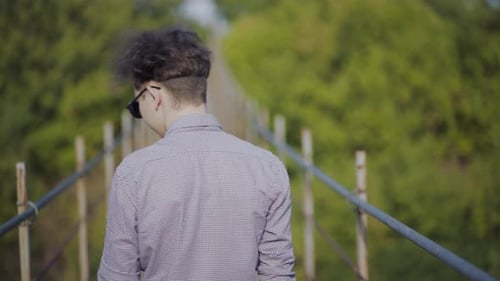 Guy Walks on Suspended Bridge in the Forest
