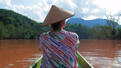 Woman with traditional hat cruising on the brown water of the Nam Ou river in La