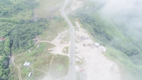 Vue aérienne d'une route rurale à voie unique sur des collines verdoyantes, vue du dessus du brouillard et des nuages pendant la saison des pluies