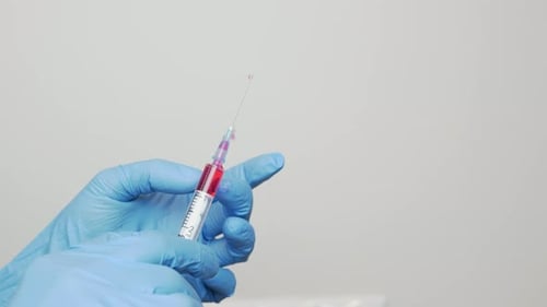 Close up of scientist doctor hands in blue disposable medical gloves with syringe with needle