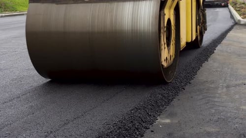 A Large Yellow Steamroller Flatten Hot Asphalt. Builds a New Road