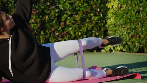 Woman Exercises with Resistance Band Outdoors on Yoga Mat