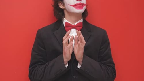 Ein Clown mit buntem Make-up posiert auf isoliertem rotem Hintergrund, ein fröhlicher Zauberer oder ein Geheimnisvoller