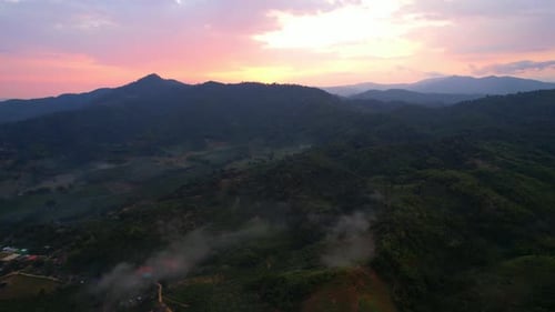 Aerial view a drone fly over a rural area with mountains in the background at sunrise.