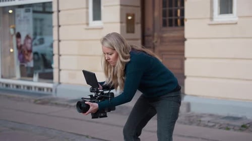 Woman Cameraman Adjusts Professional Camera on City Street