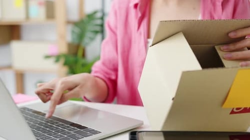 Woman using Laptop While Holding Cardboard Box