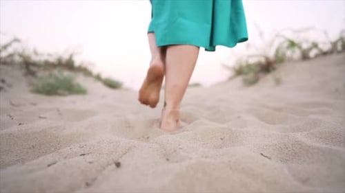 Legs of Woman Wearing Blue Skirt Walking Barefoot on Sandy Beach or Desert. Slow Motion. Girl Walks