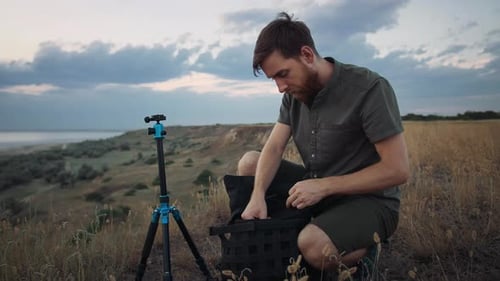Joven fotógrafo está en cuclillas en High Hill y saca la cámara de una mochila