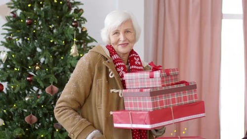 Senior Woman Holding Christmas Presents by Christmas Tree