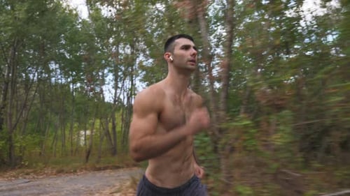 Handsome Muscular Man with Wireless Headphones Sprinting Fast Along Trail Near Forest at Early