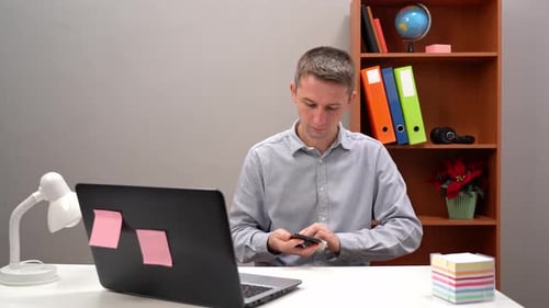 Young Guy Office Worker Manager Disinfects a Smartphone During a Pandemic