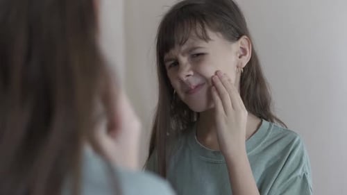 Girl Grimaces, Touching Face in Mirror