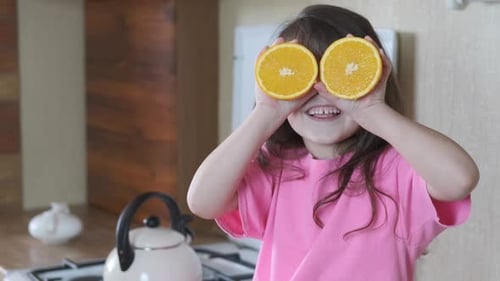 Happy Girl Plays With Orange Halves in Kitchen