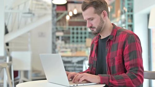 Joven enfocado usando laptop en café