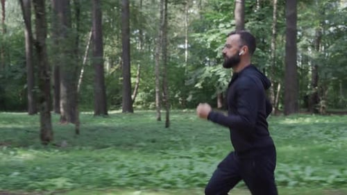 Man Running Through Summer Forest Camera Following Runner in Wireless Headphones Healthy Lifestyle