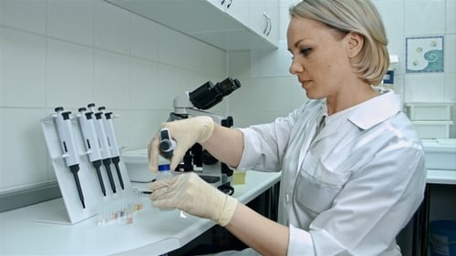 Scientist Handling Pipette with Vials and Microscope
