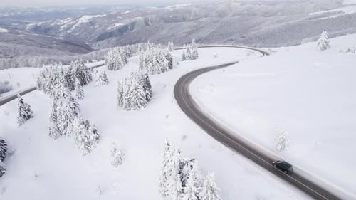 Drohne folgt schwarzem SUV, der bei winterlichen Bedingungen auf einer kurvenreichen