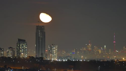 Majestic moon rising over city skyline with skyscrapers and lights