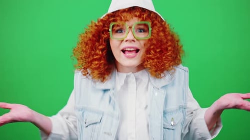 Young Redhead Curly Woman Wearing Eyeglasses and Panama Hat Outstretching Hands and Asking WHAT to