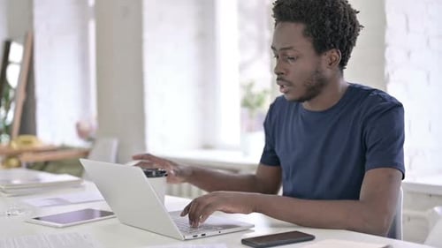 Afrikanischer Mann trinkt Kaffee während der Arbeit am Laptop