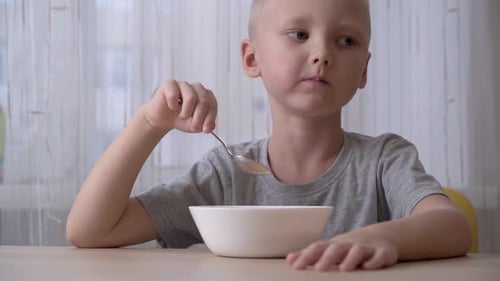Boy with Blonde Hair Eats Cereal at Table