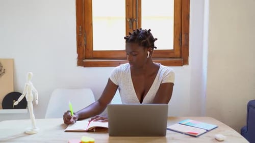 Woman at Desk Writing Next to Laptop