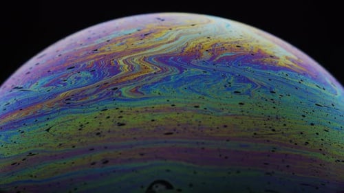 Kleine schwarze Blasen umgeben von bunten Regenbogenfarben auf Seifenfilm