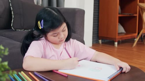 Young Girl Draws with Crayons at Table Indoors