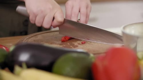 Handheld view of woman cutting chili pepper into slices