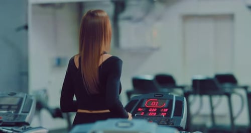 Woman with Long Hair Runs on a Treadmill in the Gym. Exercise in the Gym. View From the Back.