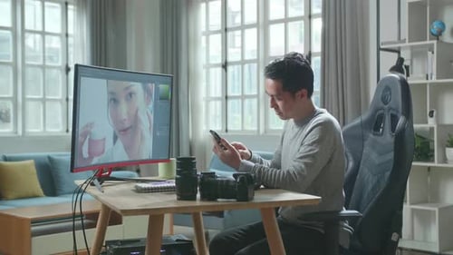 Man Using Phone at Desk With Computer Monitor