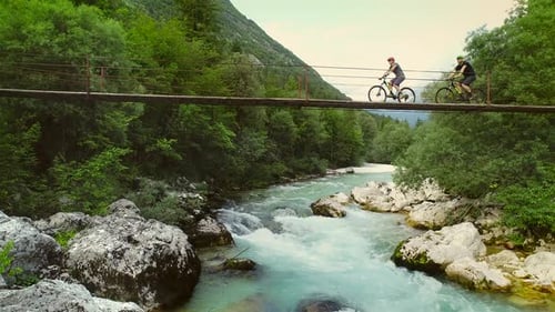 Aerial view of couple crossing a wooden bridge on bicycles at the Soca River.