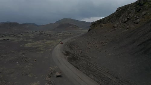 Aerial View of Fast Moving Car Driving on Dirt Road Around Mountain Ridge