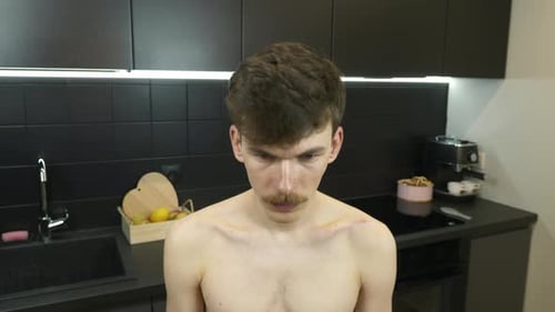 Portrait of young caucasian serious guy with mustache in the kitchen.