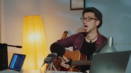 Cheerful Young Musician Playing the Guitar and Singing Into Microphone in Home Studio