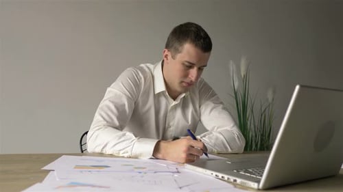 Young Adult Analyzes Business Charts at Desk