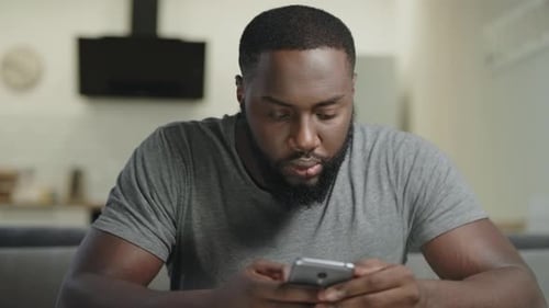 Concentrated Man Sitting with Phone. Portrait of Black Man Typing Message.