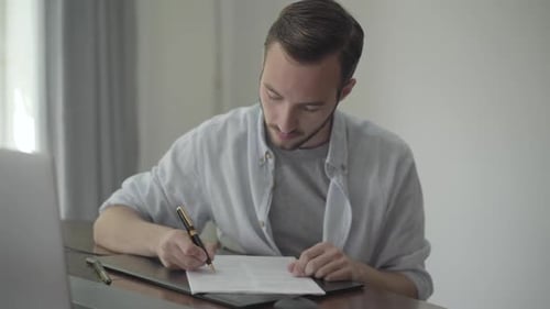 Young Writer Sitting at the Table Correcting His Essay Wrote on the Paper Using Black and Gold Pen
