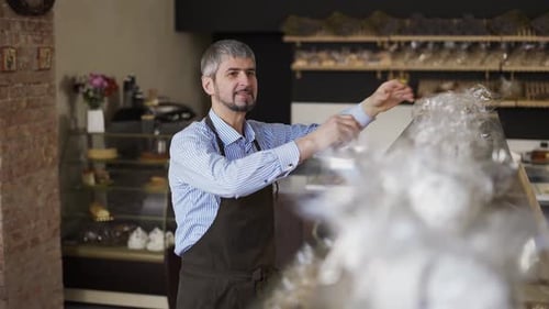 Close Up Handsome Salesman Putting Cookies on the Counter in Bakery Store
