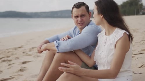 Couple Sitting on Sandy Beach Talking