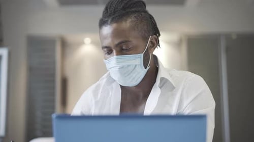 Man With Mask Working on Laptop Indoors
