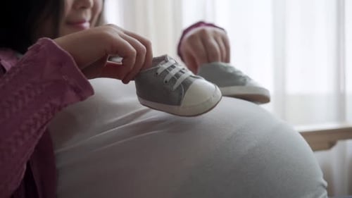 Pregnant Person Holding Baby Shoes on Belly