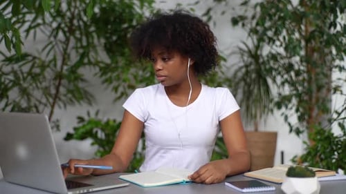 Attraktive afroamerikanische junge Frau sitzt am Schreibtisch mit Laptop Hören-Audiokurs durch